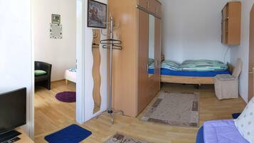 A bedroom with a bed, a wardrobe, a chair, a desk with a TV, and a door.