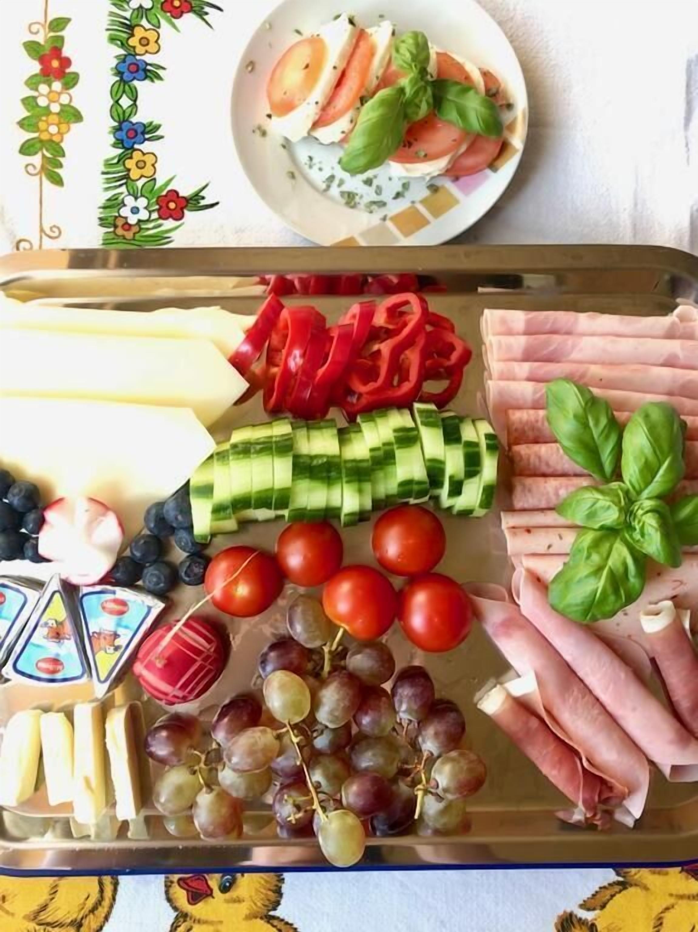 Un vassoio con diversi cibi tra cui formaggio, pomodori, cetrioli, uva e carne.
