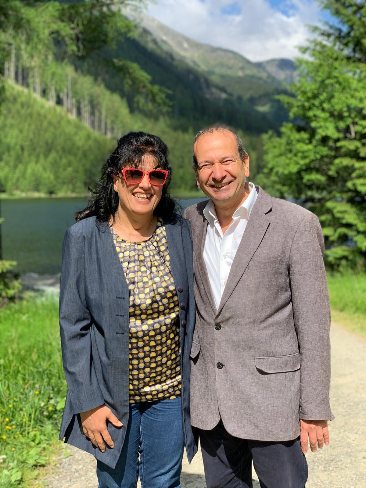 A couple standing on a path with a lake and mountains in the background.