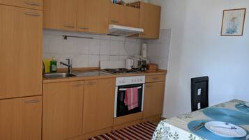 A small kitchen with wooden cabinets, a stove, a sink, and a dining area with a table set for two.