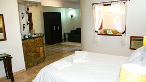 A hotel room with a bed, a stone accent wall, a bar area, and a separate seating area. - Hotel Fazenda Caluje (Engenheiro Paulo de Frontin)