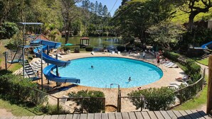 A swimming pool with a slide, surrounded by trees and a small pond. - Hotel Fazenda Caluje (Engenheiro Paulo de Frontin)