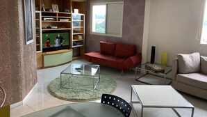 Ett vardagsrum med en tv, en röd soffa och ett soffbord i glas.