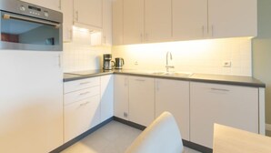 Een moderne keuken met witte kasten, een inbouwoven, een koffiezetapparaat en een spoelbak.