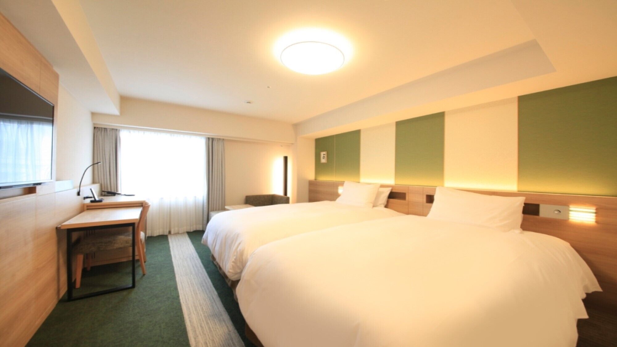 A hotel room with two beds, a desk, a chair, and a large window.