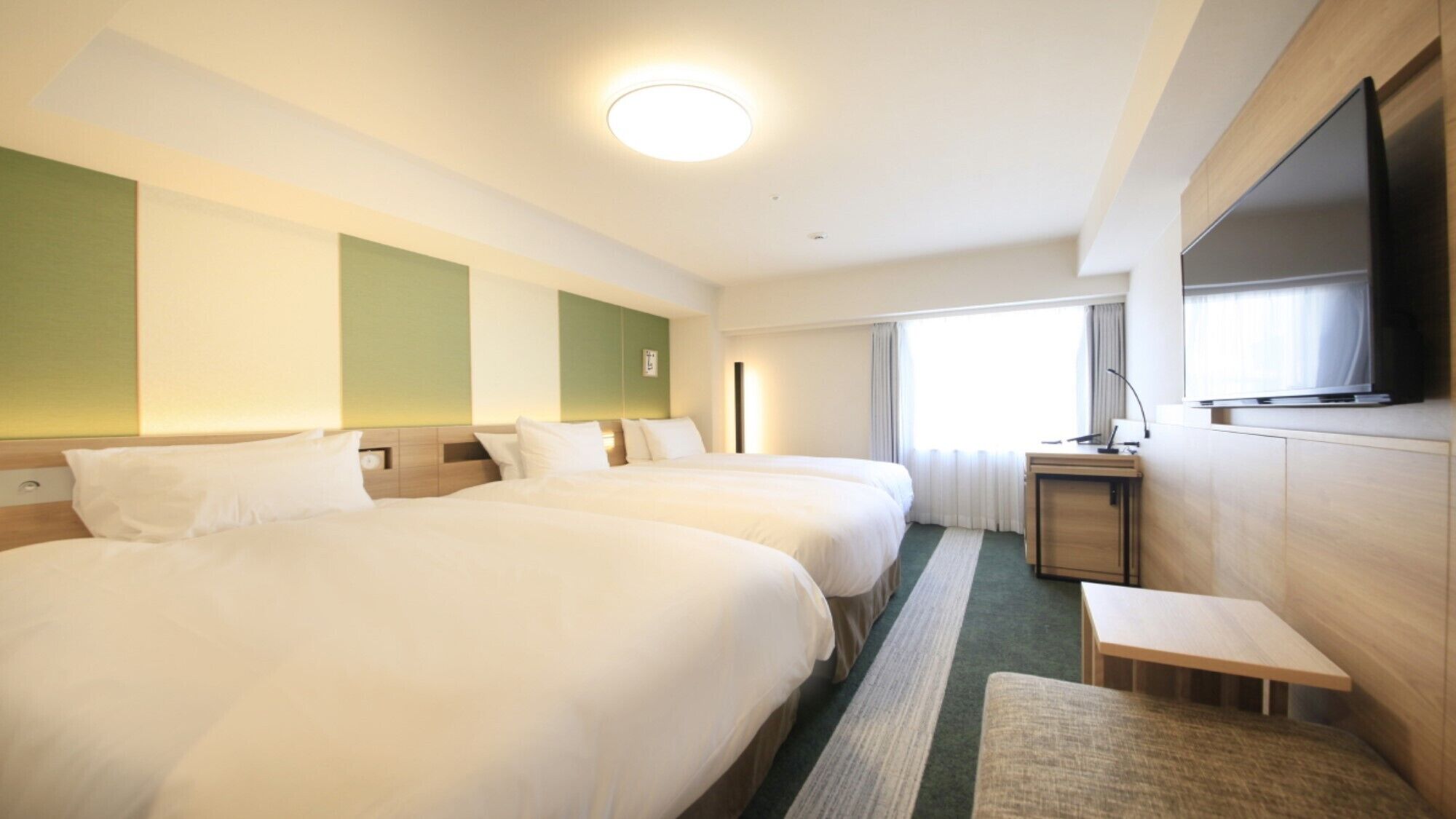 A hotel room with two beds, a TV, a small desk, and a window with curtains.