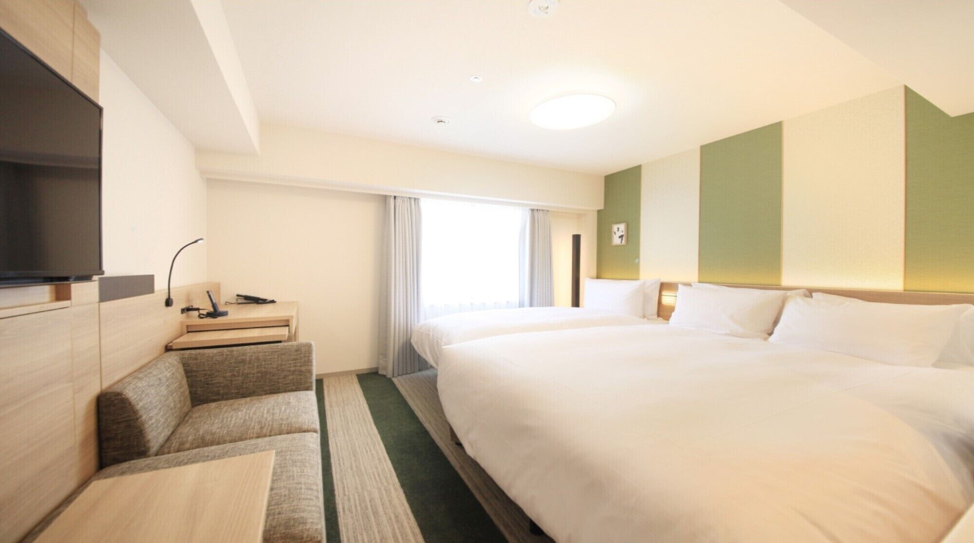 A hotel room with a large bed, a desk with a chair, a TV, and a window with curtains.