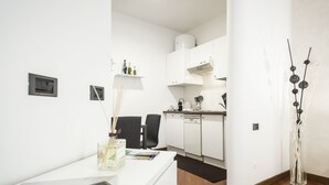 Eine moderne Küche mit weißen Schränken, einem Geschirrspüler und einer Kaffeemaschine. Es gibt einen Schreibtisch mit einer Lampe und einer Blumenvase.