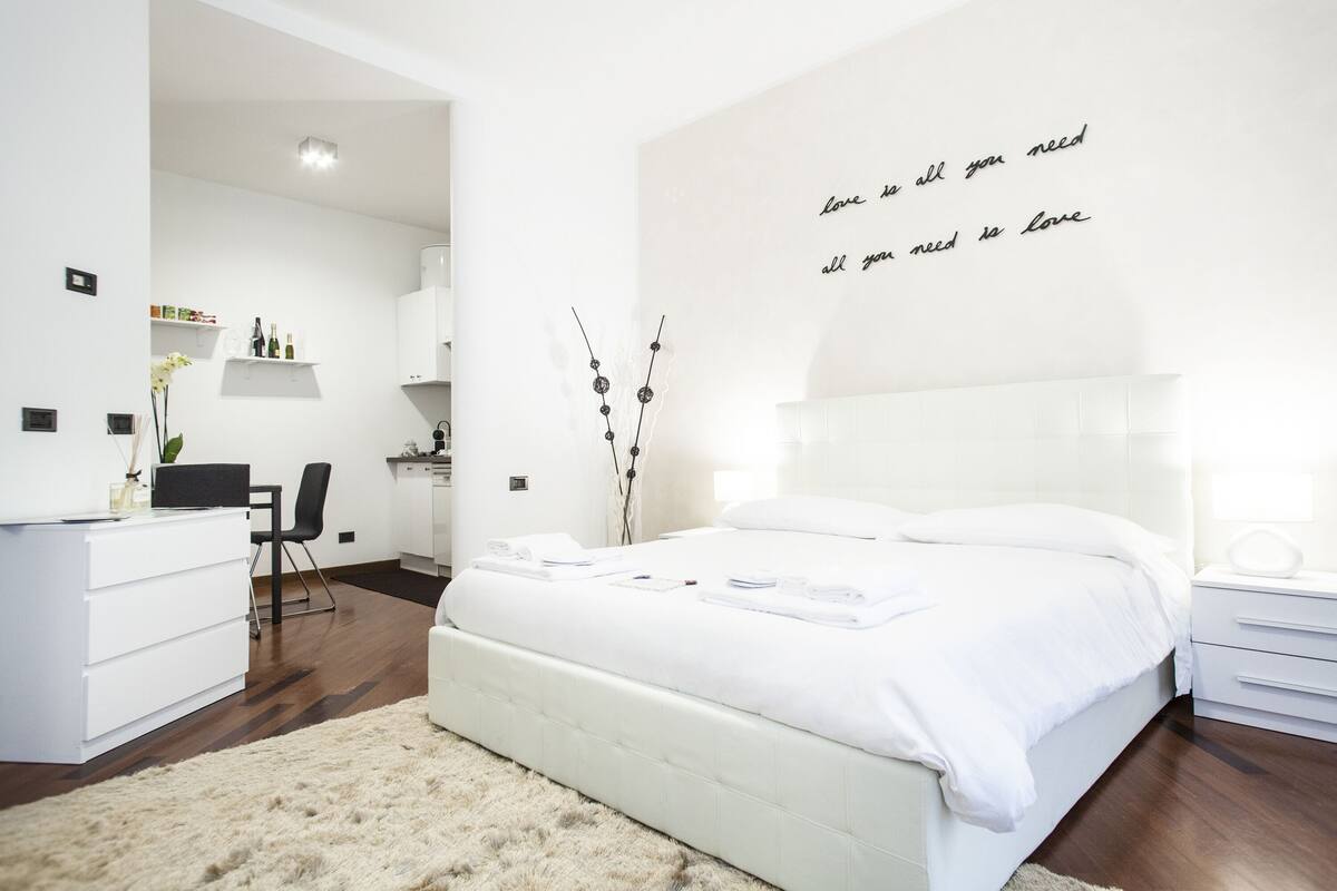 Ein modernes Schlafzimmer mit einem weißen Bett, einem Schreibtisch und einem Stuhl. An der Wand befindet sich ein motivierendes Zitat.