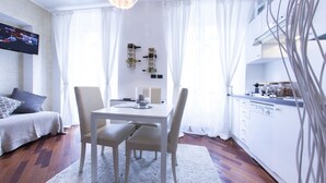 Ein modernes, helles Zimmer mit Esstisch, Stühlen, einer Couch und einer Küchenzeile.
