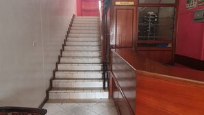 Un área de recepción con una escalera que sube a un piso superior, un mostrador de recepción de madera y un reloj en la pared.