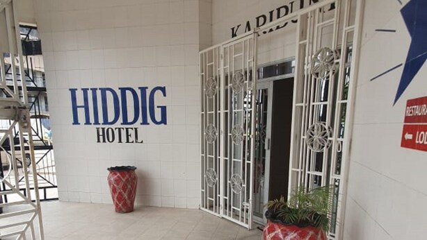 Entrada de hotel con piso de baldosas, un letrero que dice 'HIDDIG HOTEL' y una puerta con la leyenda 'KAPIDINTT'.