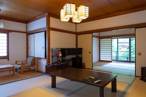 A traditional Japanese room with tatami flooring, a low table, a chair, sliding doors, and a view of greenery outside. - Koyasan Sainan-In (Koya)