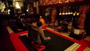 A room with a red carpet, a seated person in orange robes, and various statues and decorations.
