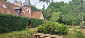 Una casa de ladrillo tradicional con una torre, rodeada de exuberante vegetación y un banco de madera.