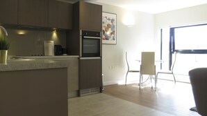 Een moderne keuken met een inbouwoven, een eethoek met tafel en stoelen, en een groot raam dat voor natuurlijk licht zorgt.