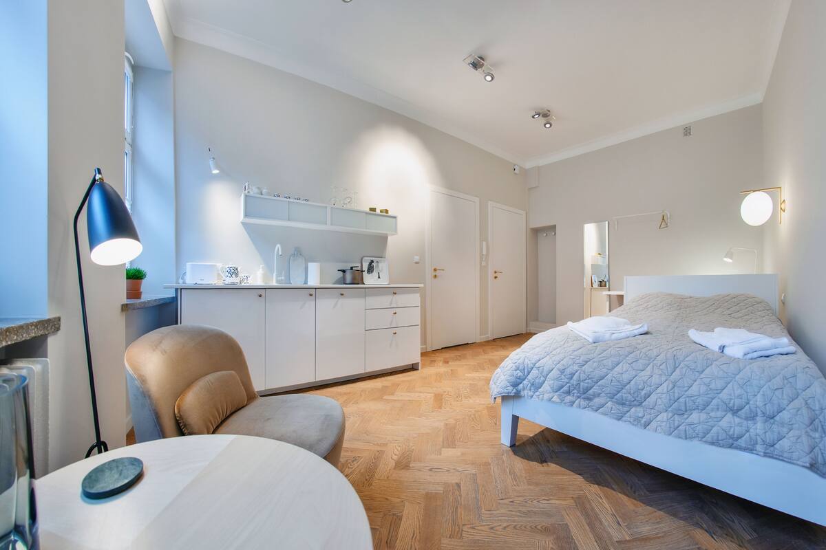 A bedroom with a bed, a chair, a desk, a dresser, and a mirror.