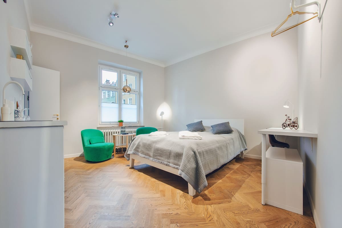 A modern bedroom with a bed, a green chair, a desk, and a radiator.