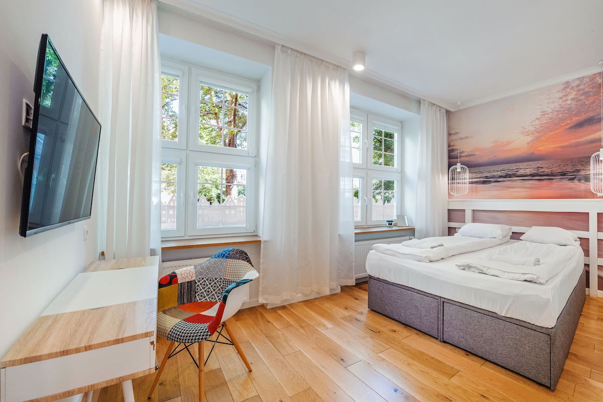 A bedroom with a bed, a TV, and a view of a sunset through the window.