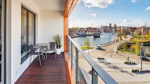 Un balcon donnant sur une rivière, avec vue sur la ville, et une petite table accompagnée de chaises.