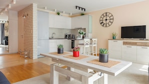 Une cuisine moderne avec des meubles blancs, une horloge et un téléviseur sur le côté droit.