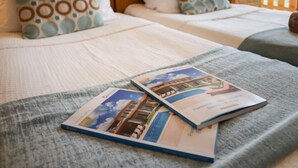 Una cama bien hecha con almohadones estampados, una manta gris y dos folletos sobre la cama.