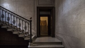 Een statige trap met versierde zwarte leuningen die naar een deur leidt.