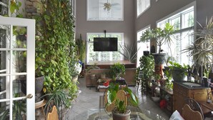 A spacious room with a high ceiling, a ceiling fan, and a large window. There is a dining table with chairs and a TV mounted on the wall. - The Lakeside Resort (Zebulon)