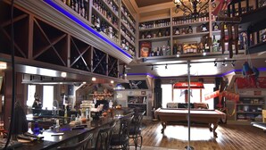 A bar area with a pool table, multiple bar stools, and a high ceiling with shelves stocked with liquor bottles. - The Lakeside Resort (Zebulon)