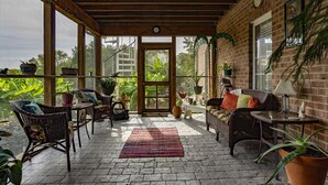A covered patio with wicker furniture, potted plants, and a brick wall. - The Lakeside Resort (Zebulon)