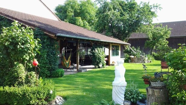 Un jardín cuidado con una estatua blanca, una casa de madera con porche y una hamaca.