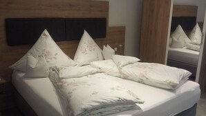 Una cama bien hecha con ropa de cama floral y varias almohadas, un cabecero de madera y un espejo que refleja la cama.