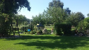 Un jardín bien cuidado con un conjunto de columpios, un pabellón y diversas plantas.