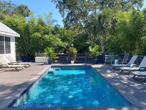 A rectangular swimming pool with blue tiles, surrounded by a wooden deck. There are lounge chairs and potted plants along the deck's perimeter.