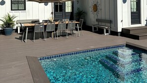 A pool area with a wooden deck, a covered patio with a table and chairs, and a building with a sign reading "SHOWERROOM ST."