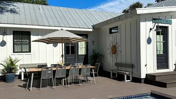 A pool area with a wooden deck, a covered patio with a table and chairs, and a building with a sign reading "SHOWERROOM ST."