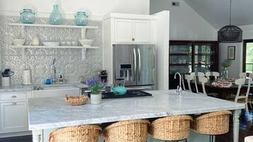 A modern kitchen with a central island, white cabinetry, and a dining area with a chandelier.
