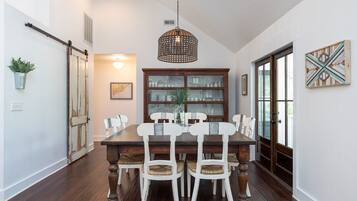 A dining room with a wooden table and white chairs, a hanging light fixture, and a glass cabinet with dishes.