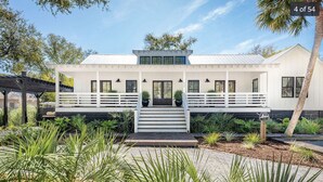 A modern two-story house with a white exterior, a covered porch, and a landscaped garden with tropical plants.