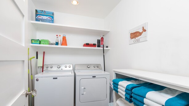 Un lavadero con dos lavadoras, un estante con productos de limpieza y un extintor de pared.