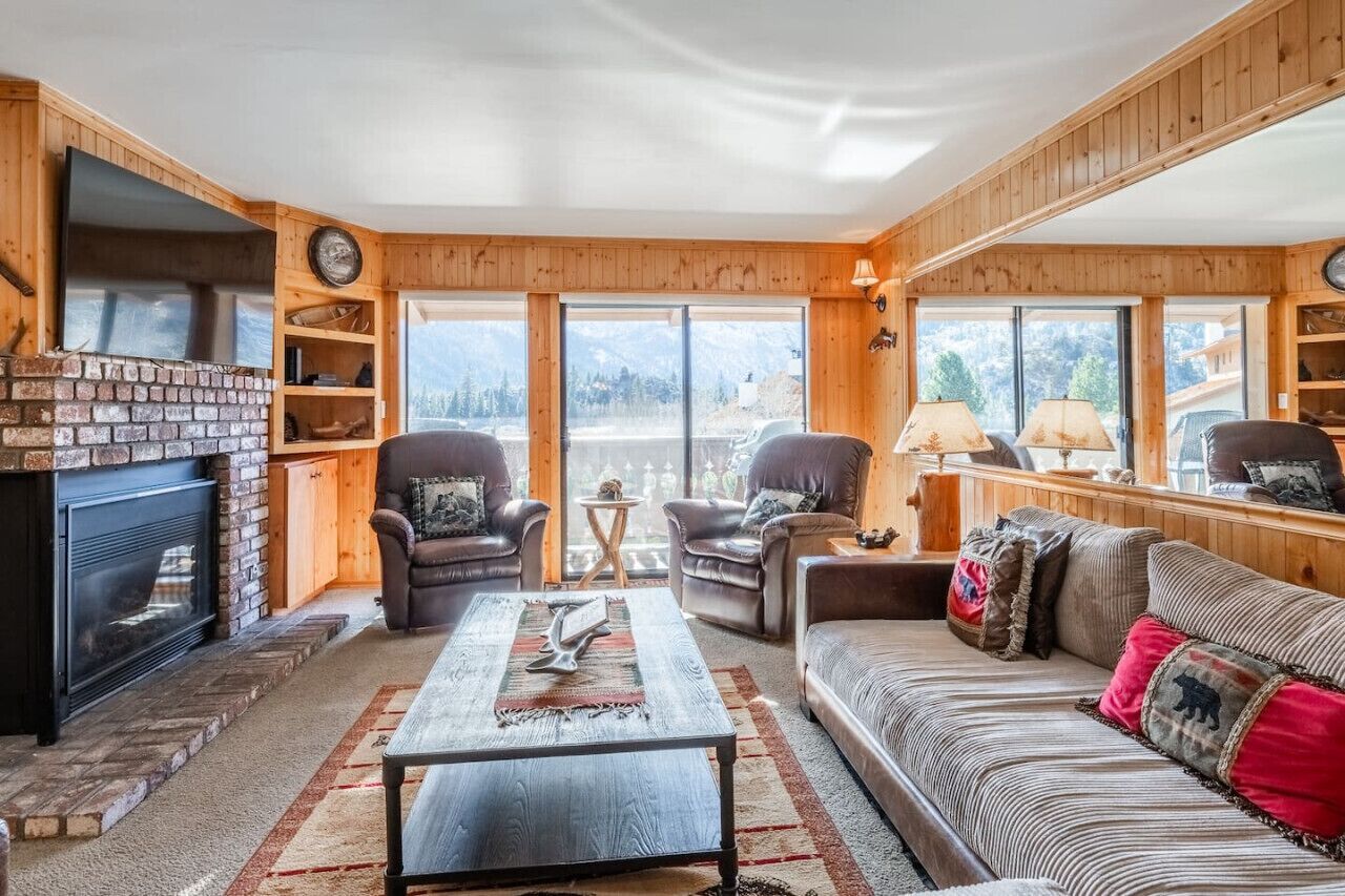 A cozy living room with a fireplace, leather sofas, and a large window offering a mountain view.