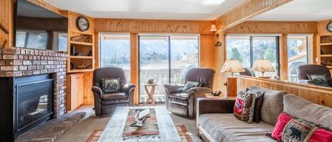 A cozy living room with a fireplace, leather sofas, and a large window offering a mountain view.