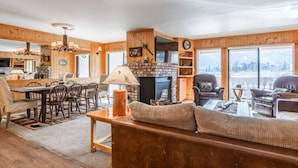 Un intérieur de chalet chaleureux avec un coin repas, une cheminée et de grandes fenêtres offrant une vue sur les montagnes.