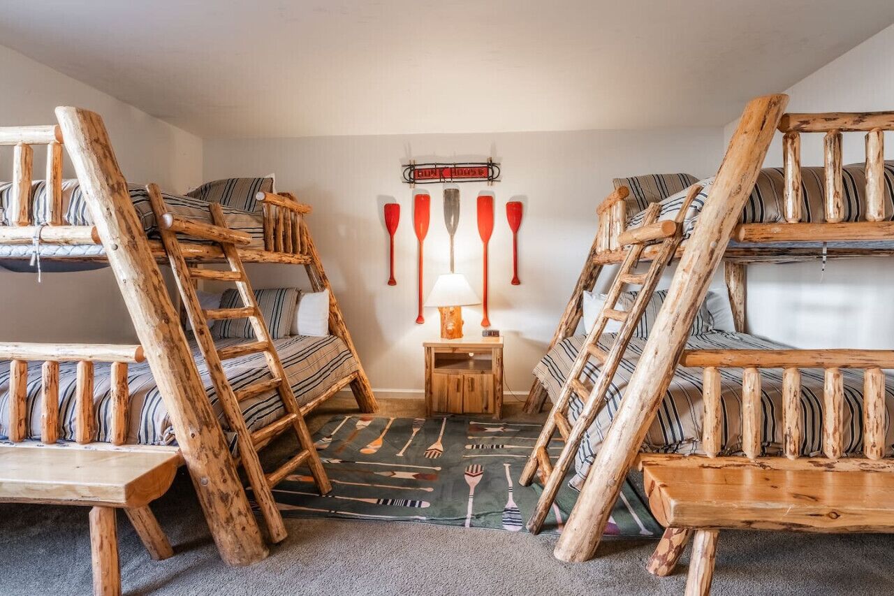 A rustic room with bunk beds, a small table, and a wall-mounted paddleboard rack.