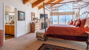Une chambre à coucher avec un lit à baldaquin, une cheminée et une grande fenêtre donnant sur les montagnes.