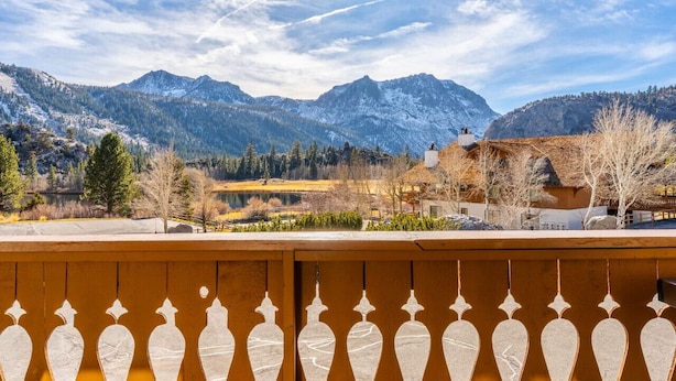 Un paysage de montagne avec des sommets enneigés, un ciel dégagé et un balcon en bois doté d’une balustrade.