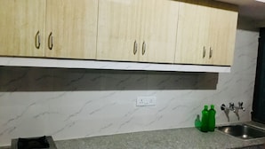 A kitchen with light wood cabinets, a marble backsplash, a gas stove, and a stainless steel sink. - 2Bedroom Set Aastha @ GIP Mall Noida (Noida)