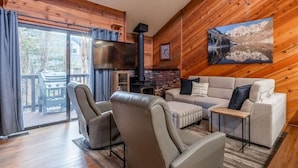 A cozy living room with a fireplace, leather chairs, a sofa, and a large window overlooking a deck. - June Lake Sierra Suns 4 -Spacious (June Lake)