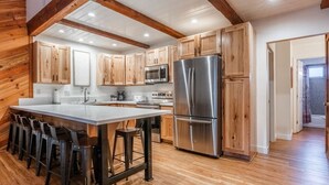 A modern kitchen with wooden cabinets, stainless steel appliances, and a bar area with stools. - June Lake Sierra Suns 4 -Spacious (June Lake)
