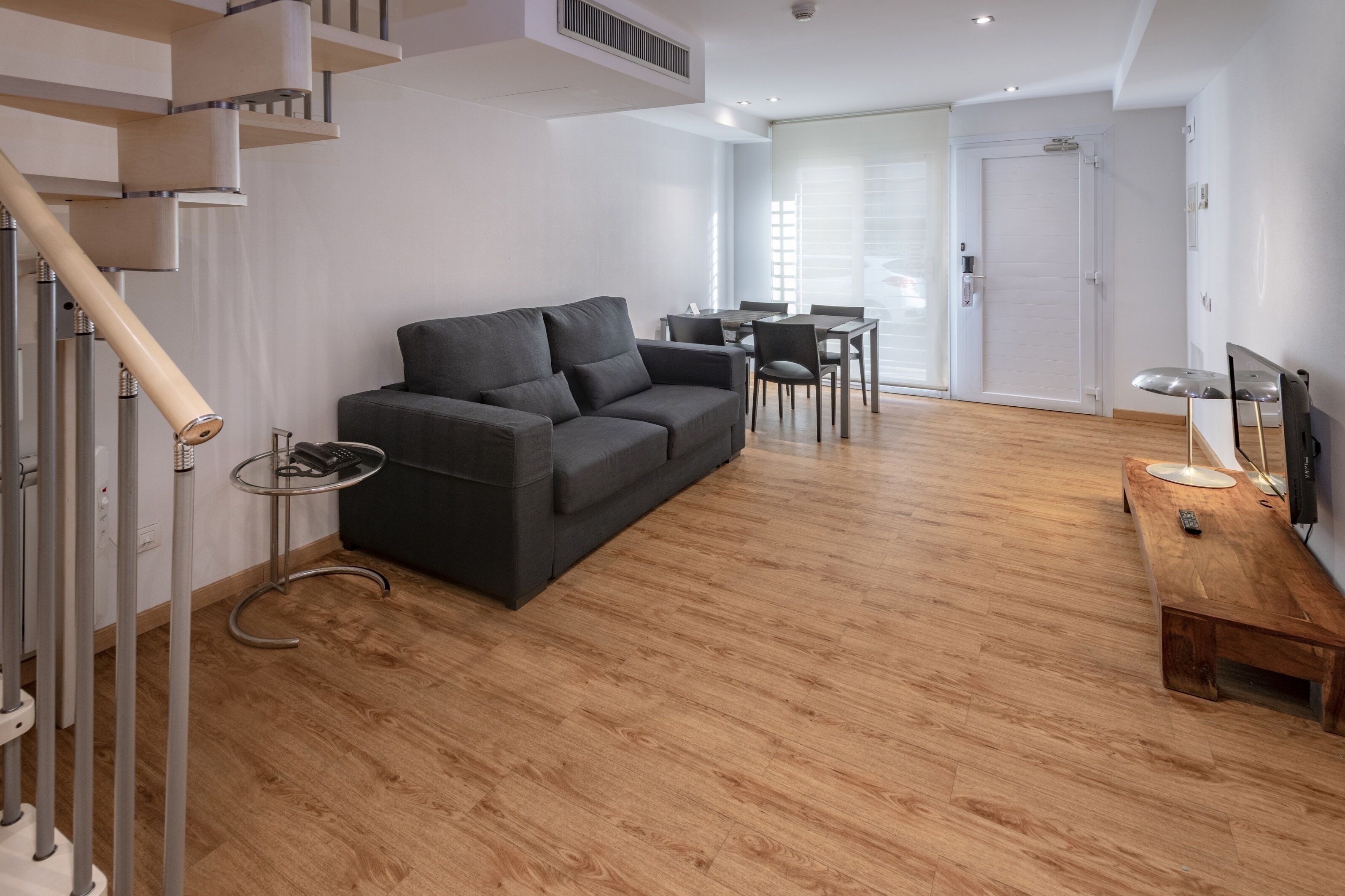 Una sala de estar moderna con un sofá, una mesa de comedor y un televisor sobre una mesa de madera.